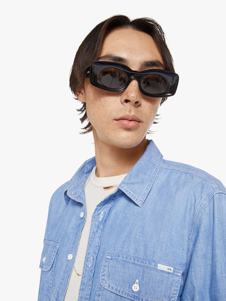 Close up view of a man in a light blue denim button-up with patch pockets, long sleeves and a curved hem.