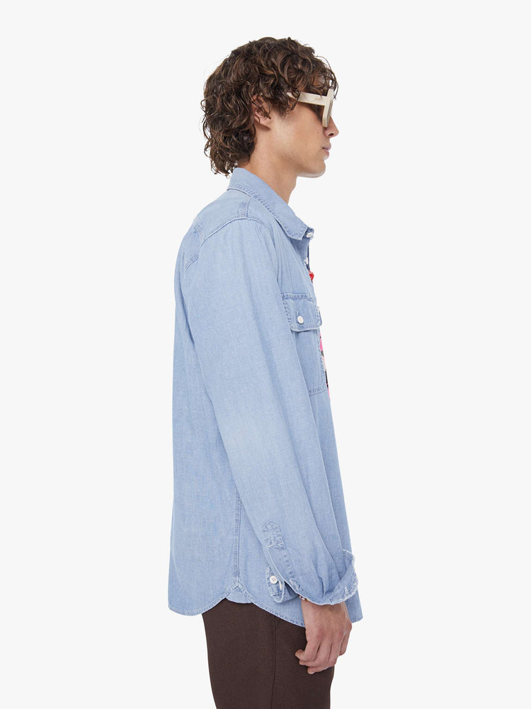 Side view of a man in light blue denim button-up with patch pockets, long sleeves and a curved hem.