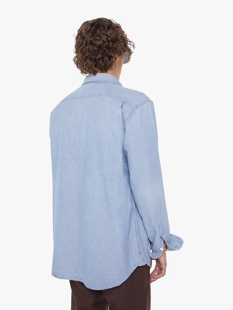 Back view of a man in light blue denim button-up with patch pockets, long sleeves and a curved hem.