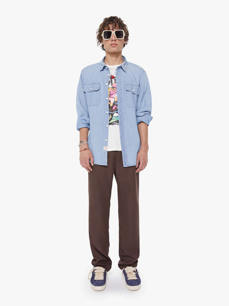 Full body view of a man in light blue denim button-up with patch pockets, long sleeves and a curved hem.