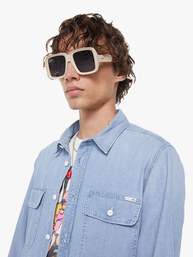 Close up view of a man in light blue denim button-up with patch pockets, long sleeves and a curved hem.