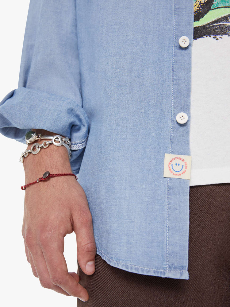 Swatch view of a man in light blue denim button-up with patch pockets, long sleeves and a curved hem.