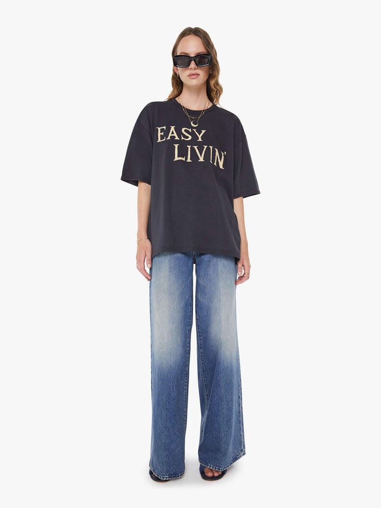 WOMAN full body view faded black tee features an oversized yellow text graphic on the front.