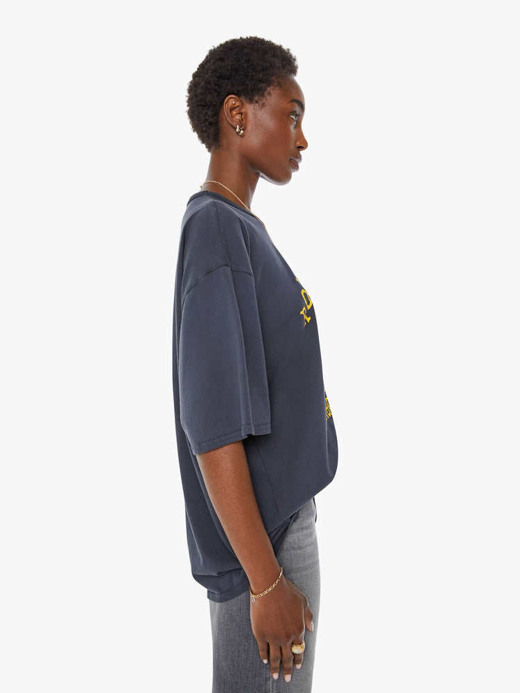 WOMAN side view in a faded black tee with a yellow graphic on the front inspired by a dirt bike racing team.