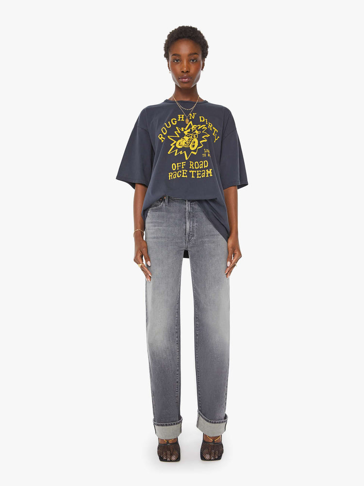 WOMAN full body view in a faded black tee with a yellow graphic on the front inspired by a dirt bike racing team.