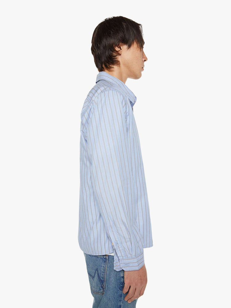 Side view of a man in a light blue, black and white stripe classic button-up with a loose fit and slightly cropped hem.