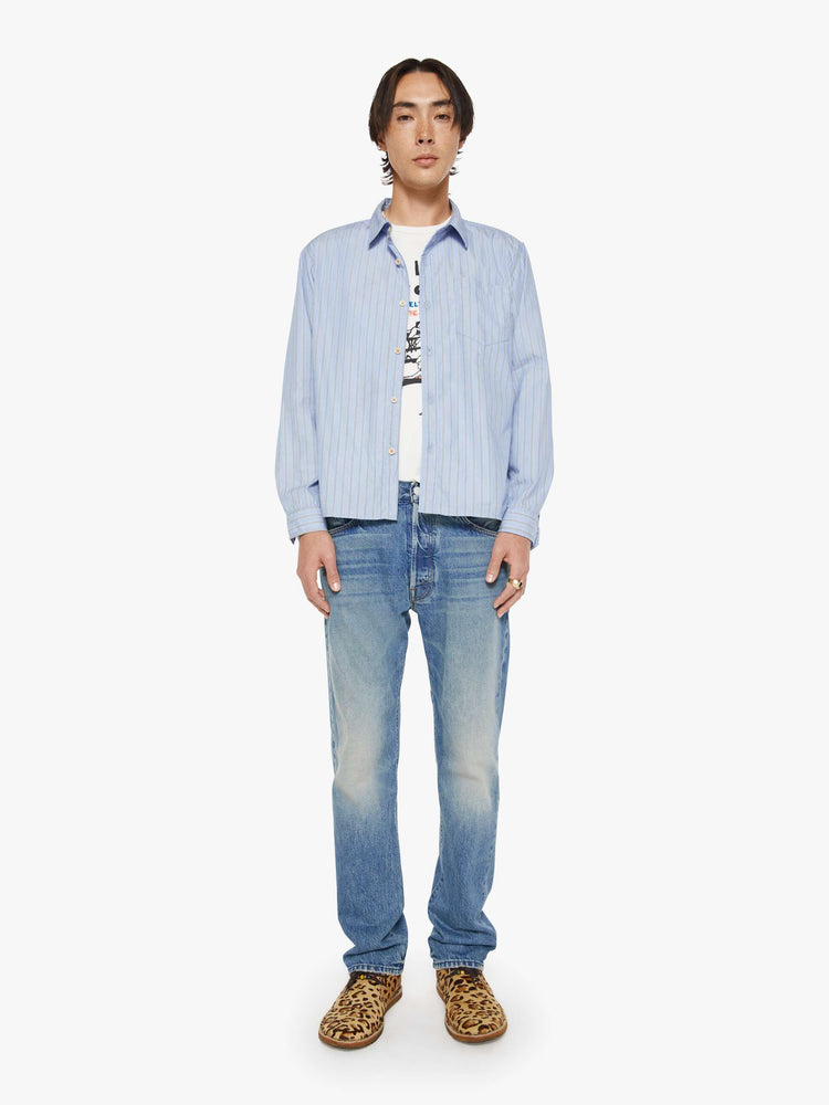 Full body view of a man in a light blue, black and white stripe classic button-up with a loose fit and slightly cropped hem.