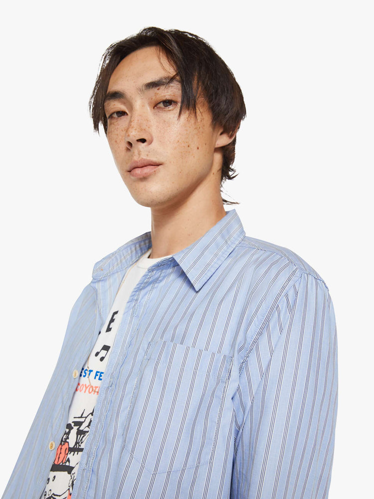Close up view of a man in a light blue, black and white stripe classic button-up with a loose fit and slightly cropped hem.