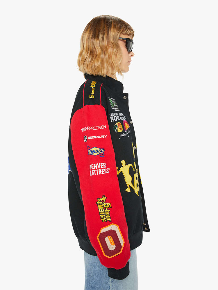 Side image of a woman wearing a racer jacket in black and red featuring various patches.