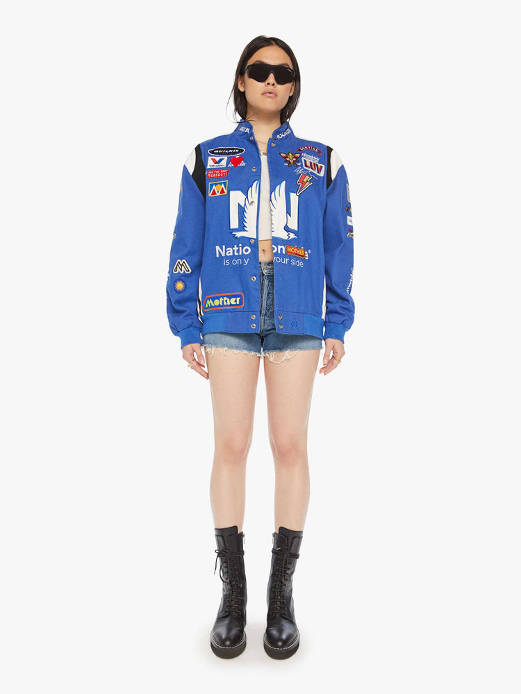 Front full body image of a womens blue racer jacket featuring assorted patches.