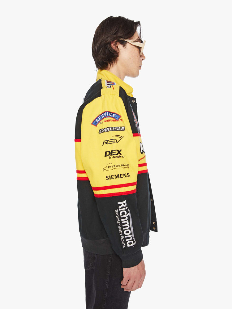 Side view of a men's racing jacket with drop shoulders, ribbed hems, snaps down the front and an oversized fit one of one combination of colors and patches inspired raceway logos.