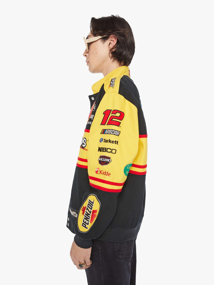 Left side view of a men's racing jacket with drop shoulders, ribbed hems, snaps down the front and an oversized fit one of one combination of colors and patches inspired raceway logos.
