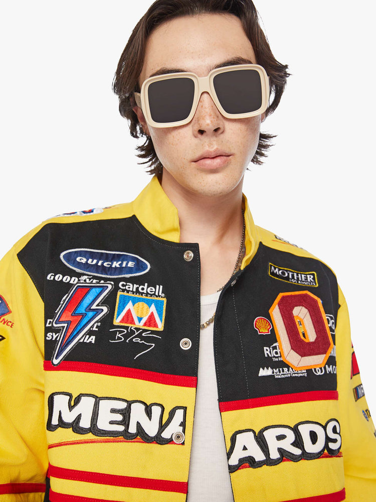 Close up view of a men's racing jacket with drop shoulders, ribbed hems, snaps down the front and an oversized fit one of one combination of colors and patches inspired raceway logos.