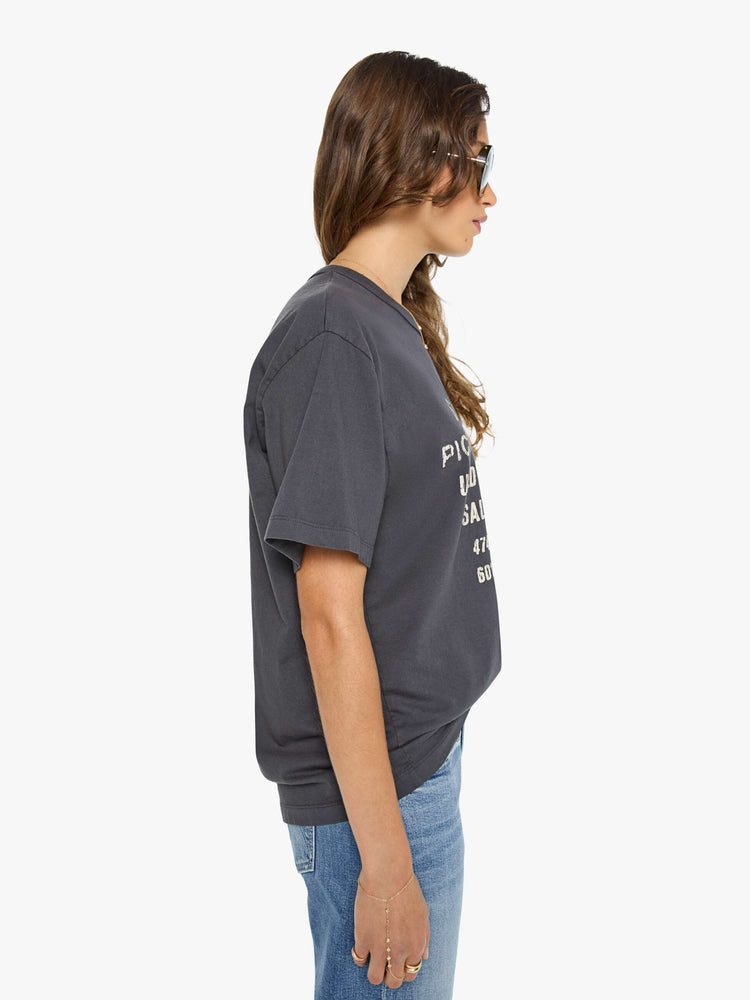 WOMAN side view in a dark grey oversized tee features a crackled text graphic and pickup truck in white on the front.