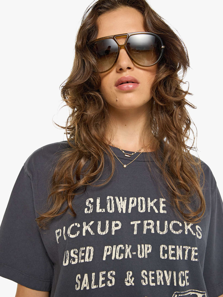 WOMAN close up view in a dark grey oversized tee features a crackled text graphic and pickup truck in white on the front.