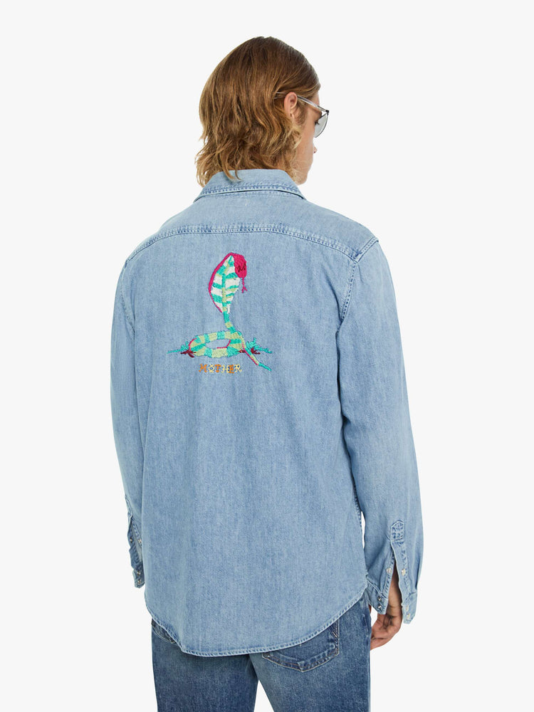 Back view of a man in a light blue with pearl snap buttons, fading at the shoulders and tigers embroidered on the chest classic button-up shirt with front patch pockets, a curved hem and slightly oversized fit. 