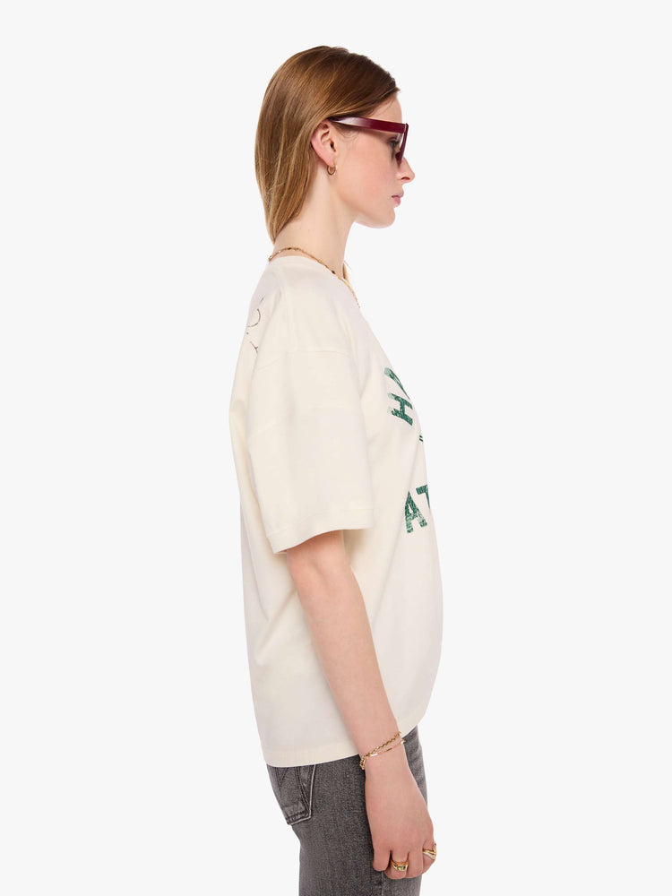 WOMAN side view of an off-white tee with a faded, vintage-inspired green football graphic with text on the front.