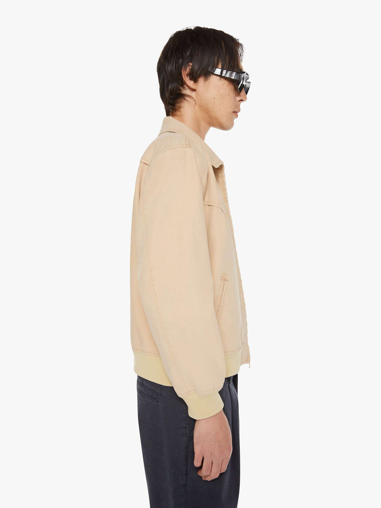 Side view of a man in a light khaki boxy zip-up rain jacket with a Western-inspired yoke, slit pockets, elastic hems and a slightly cropped fit.