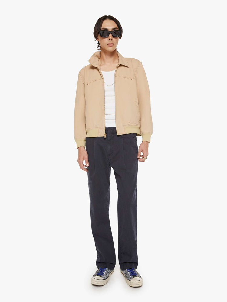 Full body view of a man in a light khaki boxy zip-up rain jacket with a Western-inspired yoke, slit pockets, elastic hems and a slightly cropped fit.