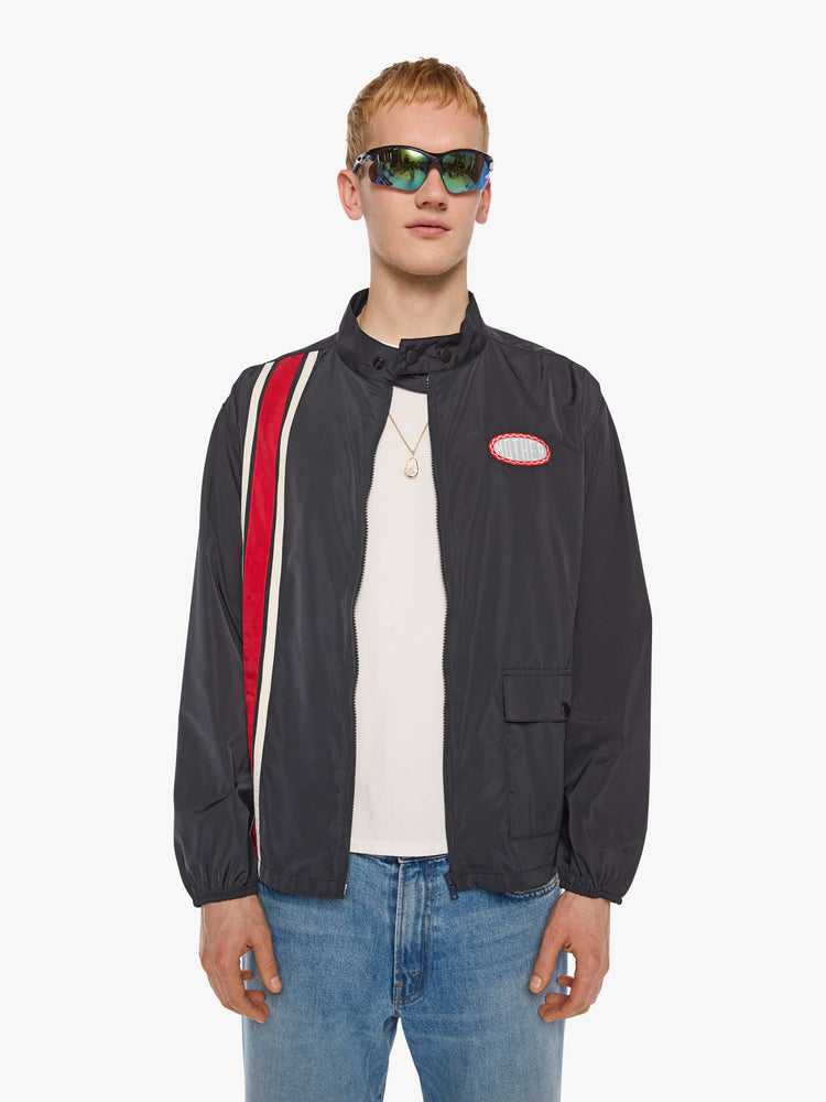 Front view of a man in a black with red and white stripes down the front jacket with a stacked collar that snaps, a low front patch pocket and elastic hems. 