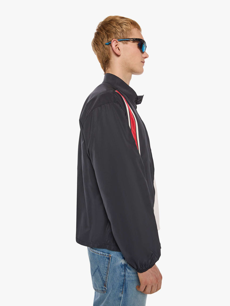 Side view of a man in a black with red and white stripes down the front jacket with a stacked collar that snaps, a low front patch pocket and elastic hems. 
