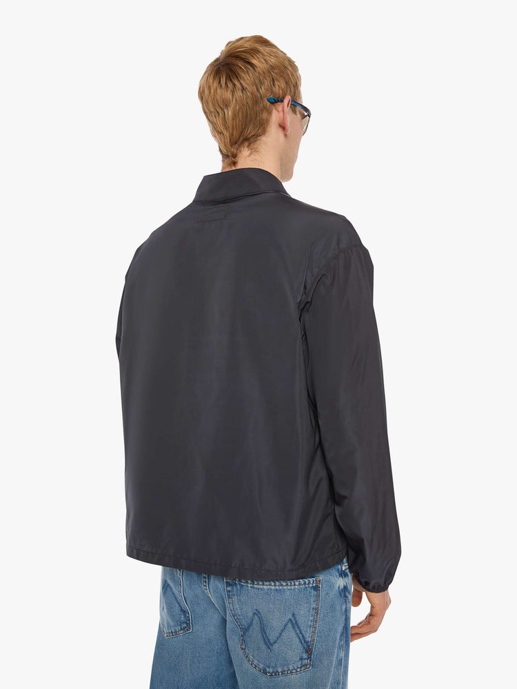 Back view of a man in a black with red and white stripes down the front jacket with a stacked collar that snaps, a low front patch pocket and elastic hems. 