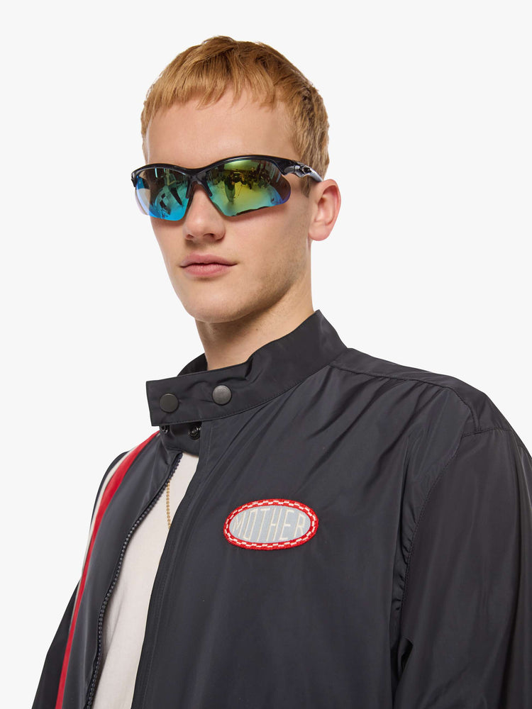 Close up view of a man in a black with red and white stripes down the front jacket with a stacked collar that snaps, a low front patch pocket and elastic hems. 
