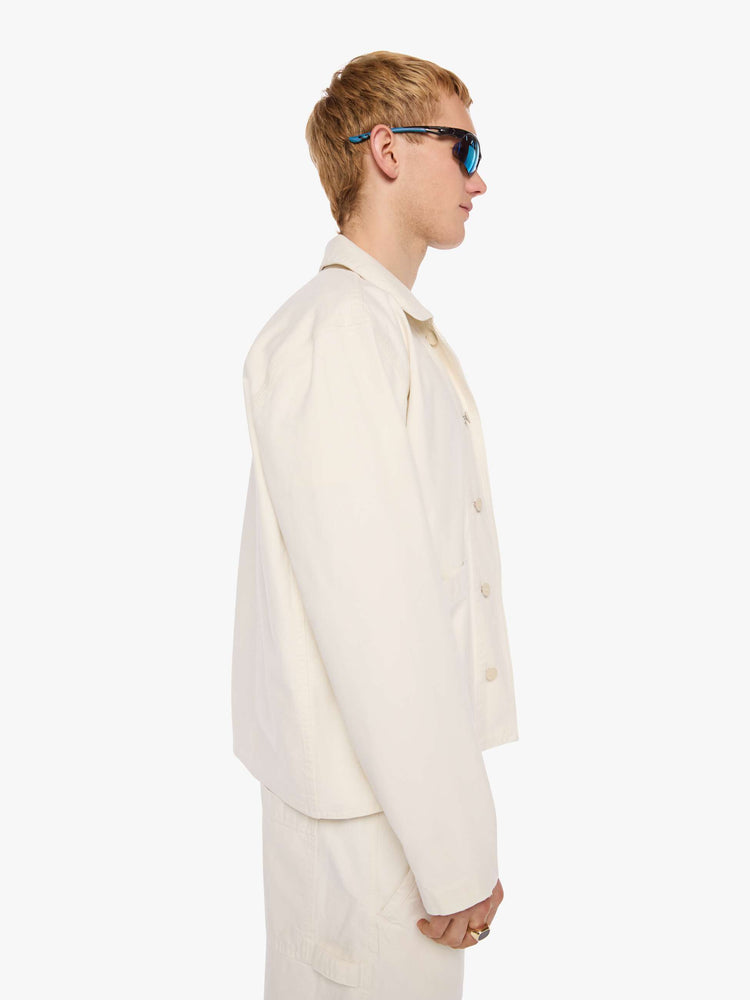 Side view of a man in a jacket designed in cream with tonal buttons down the front.