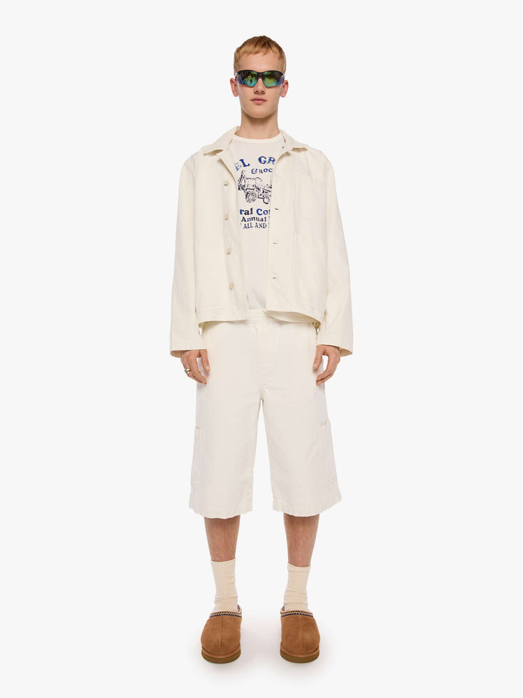 Full body view of a man in a jacket designed in cream with tonal buttons down the front.