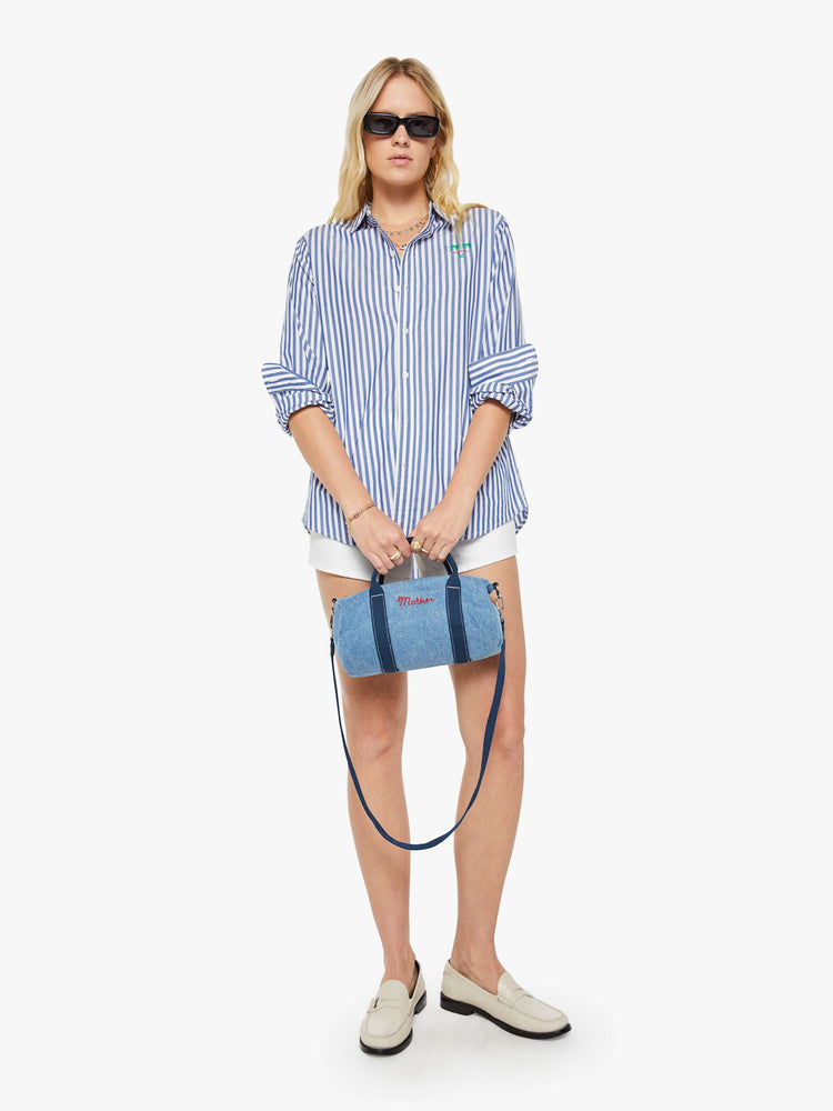 Woman holding view of a faded blue with navy stripes and MOTHERS name embroidered in red across the front  mini bag with a top handle, optional shoulder strap and duffle-bag inspired design. 