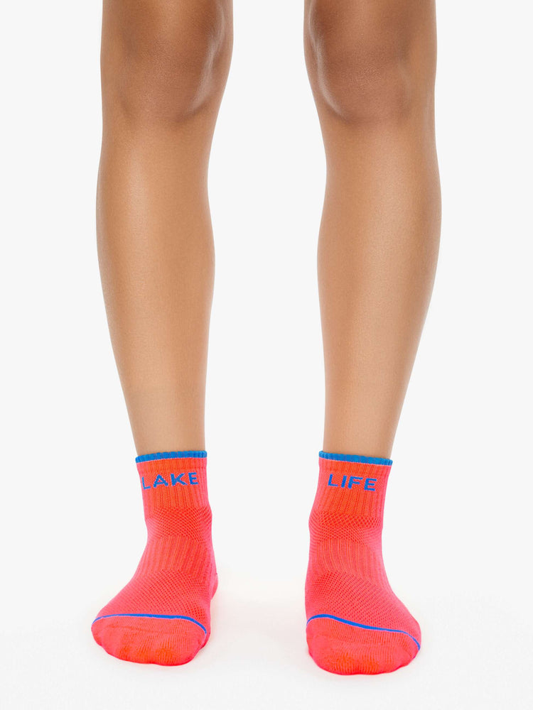 On model ankle-length tube socks designed in neon orange with blue text and details.