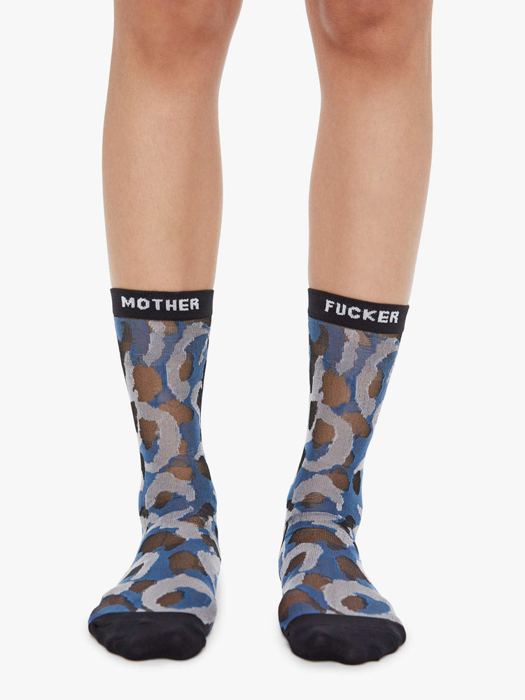 On model view of classic tube socks with an explicit message from MOTHER. The socks are designed in a translucent blue, grey and tan oversized leopard print with black trim and text in white.