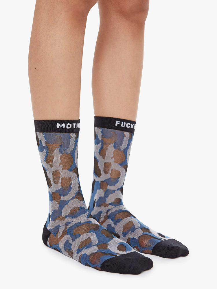 On model view of classic tube socks with an explicit message from MOTHER. The socks are designed in a translucent blue, grey and tan oversized leopard print with black trim and text in white.