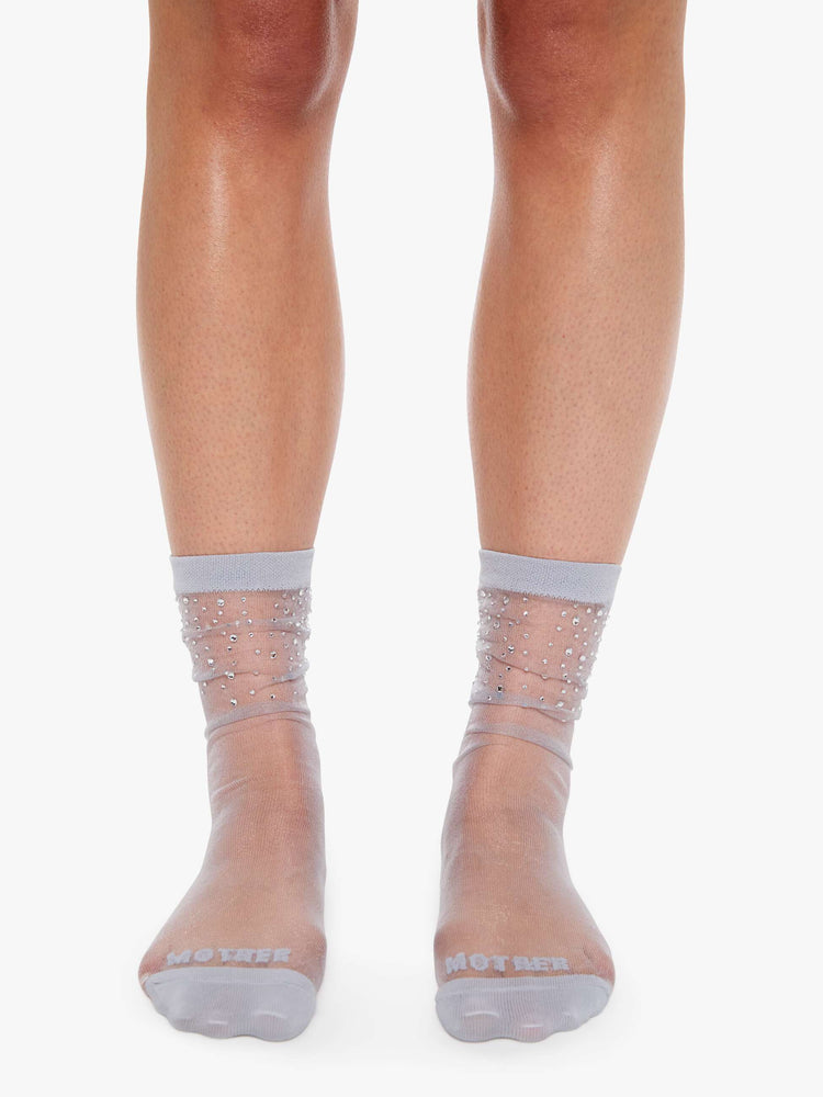 Front view on a model tube socks designed in a sheer grey fabric with rhinestones at the ankle and MOTHER's name printed across the toes.