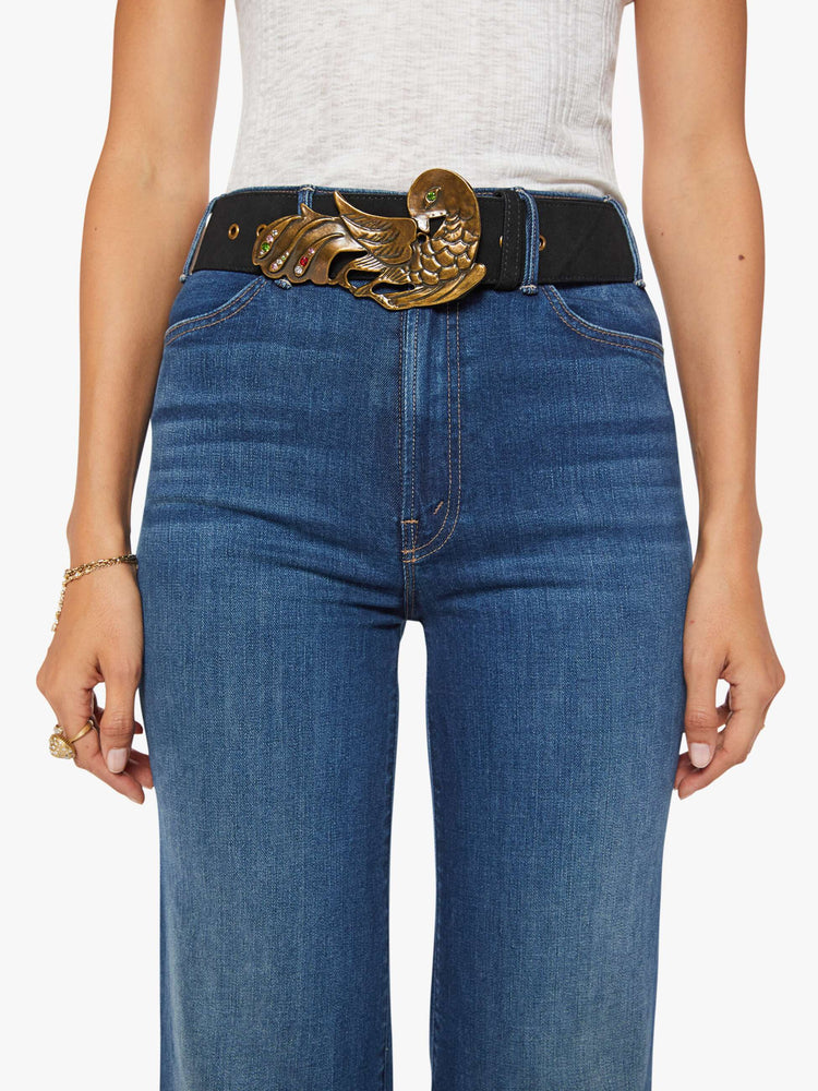 On model view of a wide leather belt designed in black suede with an oversized antique brass buckle detailed with colored gemstones.