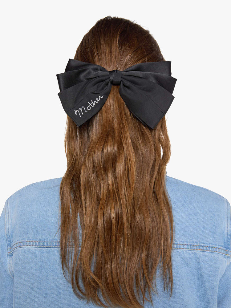 On model view of a woman in a black hair bow that fastens with a metal barrette so you can clip it on.