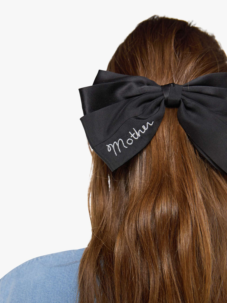 Close up view of a woman in a black hair bow that fastens with a metal barrette so you can clip it on.