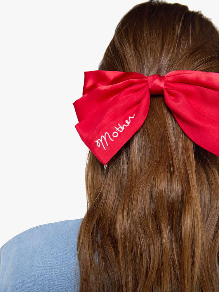 Close up on model view of a woman in a red hair bow that fastens with a metal barrette so you can clip it on.