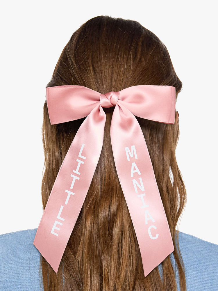 On model pink, satin-feel hair bow that looks sweet but says otherwise—with LITTLE on one tail and MANIAC on the other.