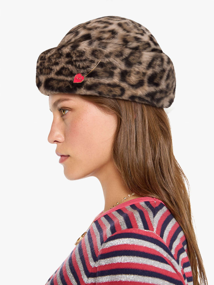 Side view of a woman in a hat with a wide folded brim and a decorative gold-toned pin with a pink heart.