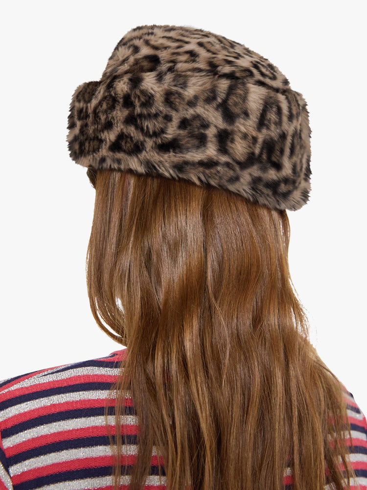 Back view of a woman in a hat with a wide folded brim and a decorative gold-toned pin with a pink heart.