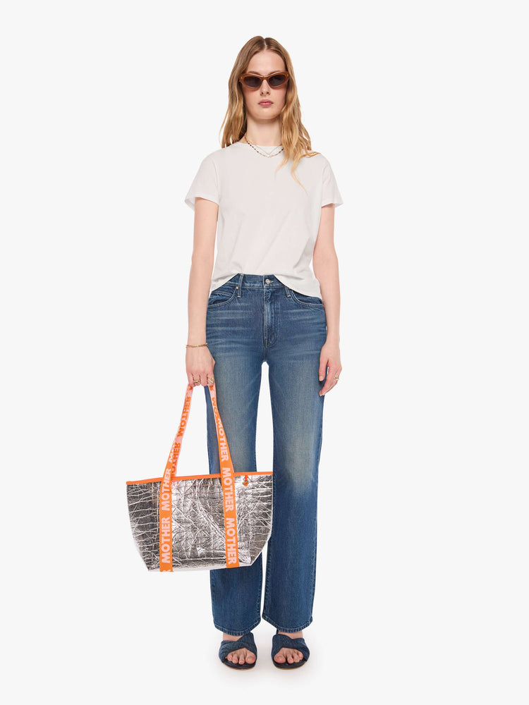 On model view metallic silver with a branded orange-and-baby-pink strap and decorative heart charm, and measures 11-inches wide and 10-inches tall with a 5 1/2-inch gusset.