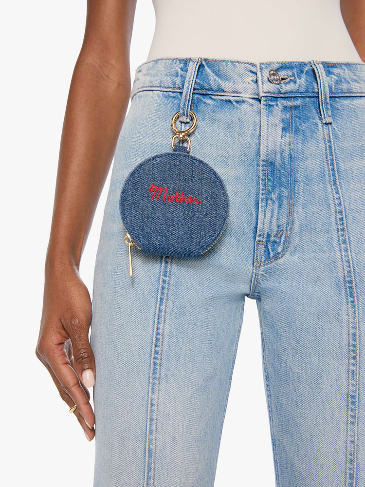 Front view of a woman wearing a classic blue denim with MOTHER embroidered across the front in red, a zip closure and a 1-inch key ring.
