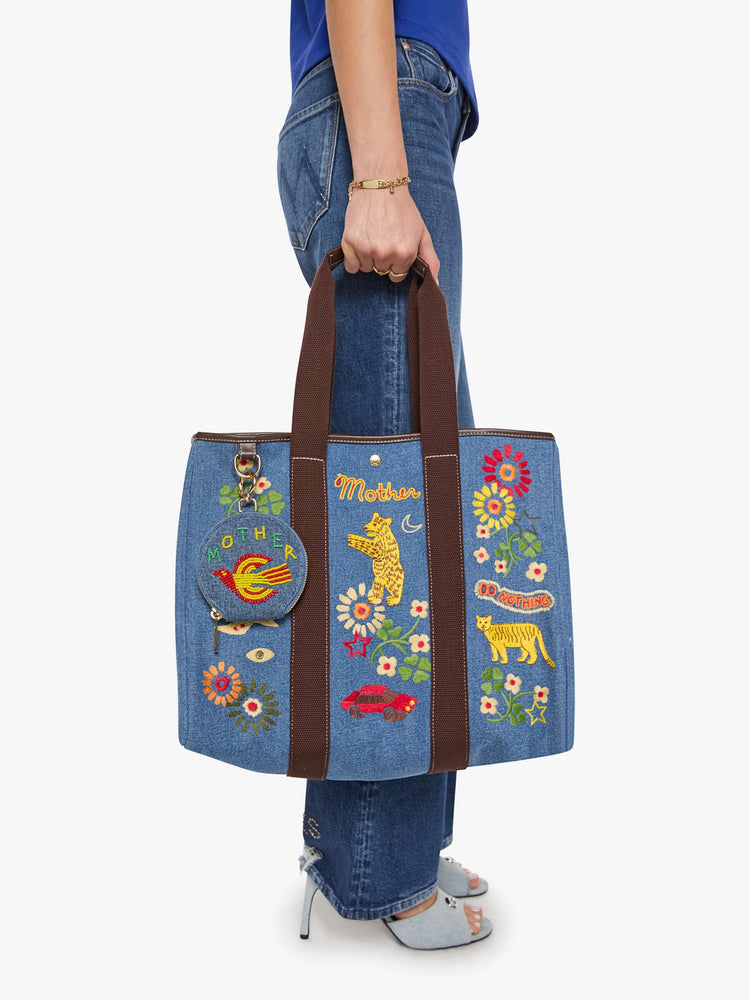 On bag view of a wallet in a classic blue denim with a flying bird and MOTHER's name in green, yellow and red beads across the front, a zip closure and a 1-inch key ring.