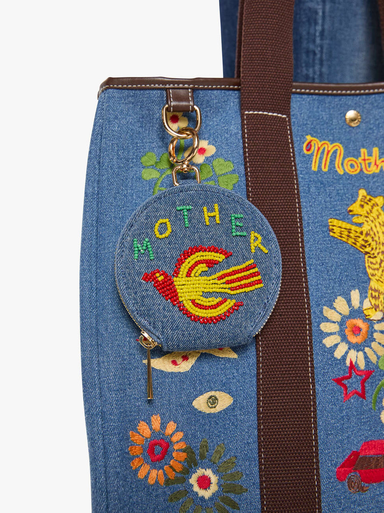 Close up of a bag view of a wallet in a classic blue denim with a flying bird and MOTHER's name in green, yellow and red beads across the front, a zip closure and a 1-inch key ring.