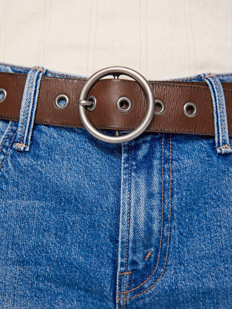 On model  view of a dark brown vintage-inspired belt with an oversized circular buckle and round rivets throughout.