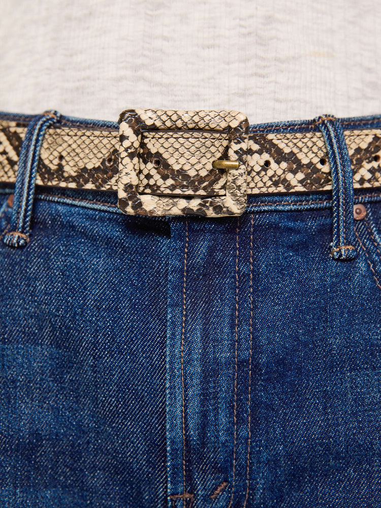 Close up on model  view of a belt designed in faux snakeskin with an oversized rectangular buckle. 