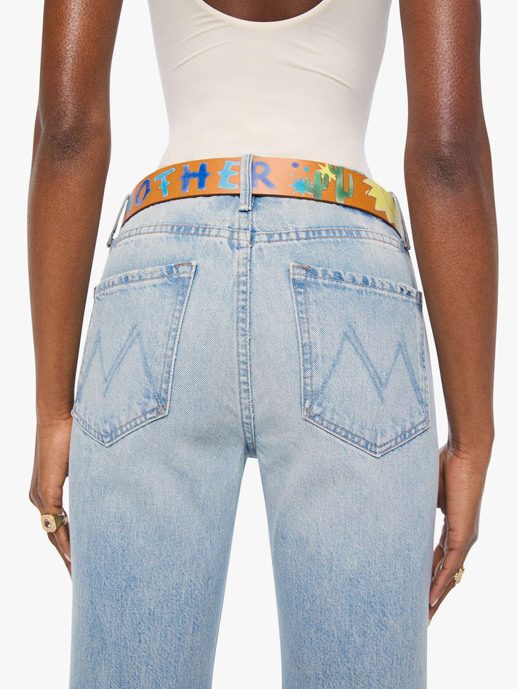 On model view  belt made from 100% leather in tan with hand-painted stars, mushrooms and rainbow stripes, and an oversized brass buckle.