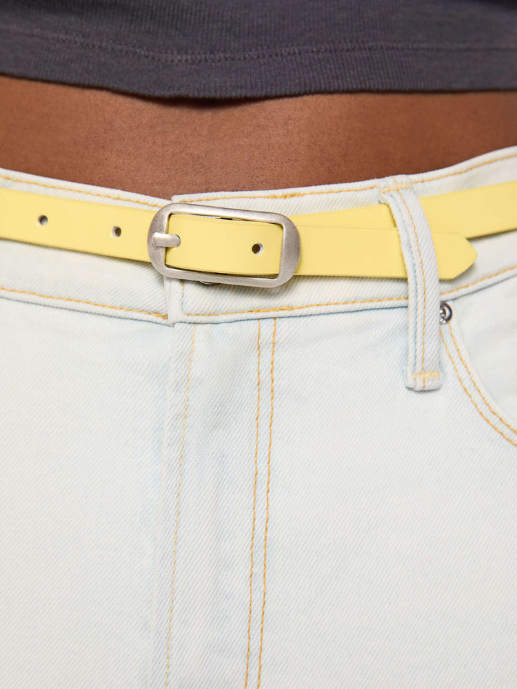 Close up on model view of a narrow belt is made from 100% leather with a pastel yellow coating and silver hardware.