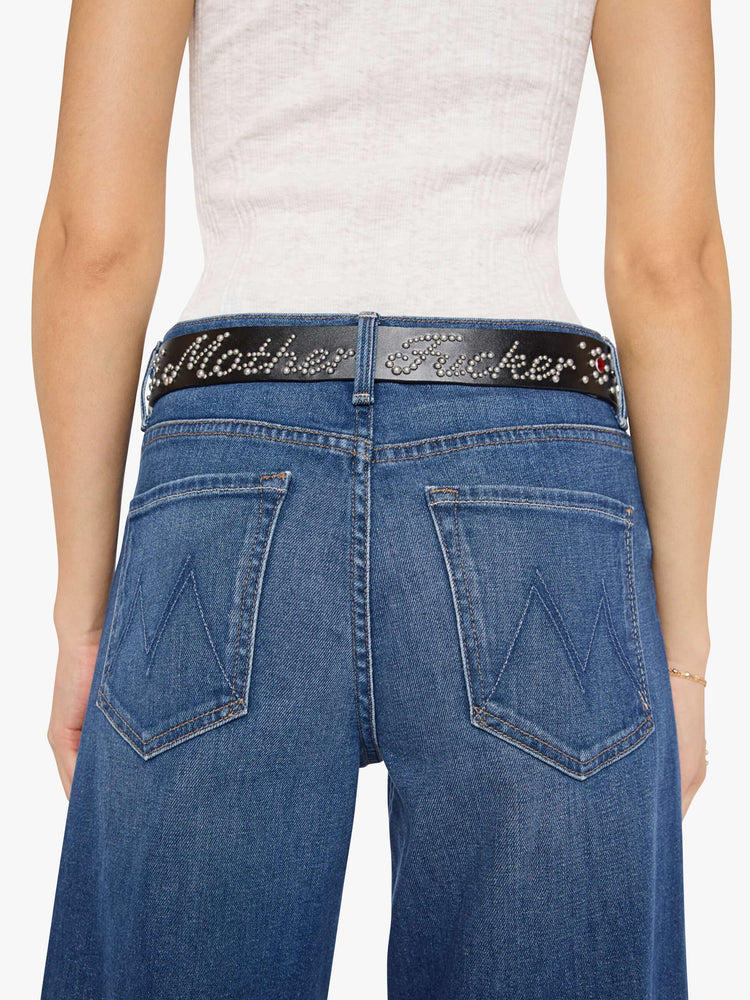 On model view of a woman in a  wide belt made from 100% leather in black with an oversized metal buckle, studded stars, rhinestone details and an explicit message across the back.
